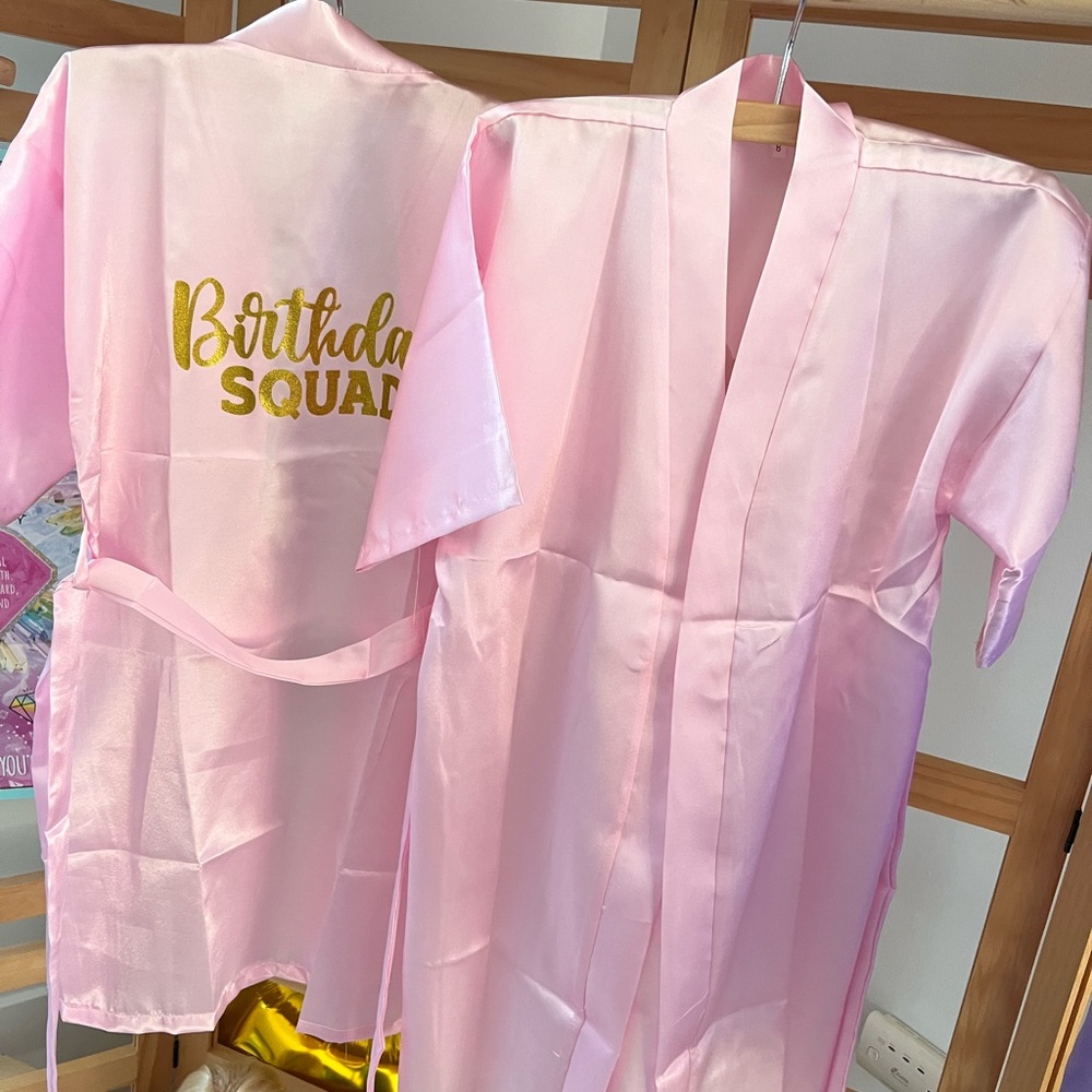 Two pink “Birthday Squad” spa party robes and acessories